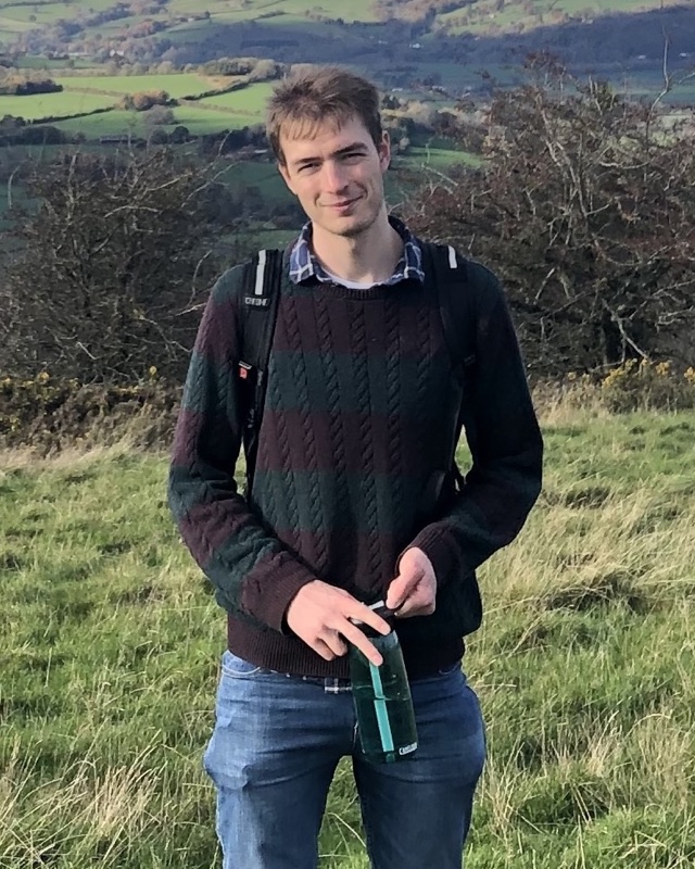 Max Carter-Brown standing on a grassy hillside above a patchwork of fields